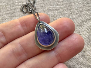 Hand-set, polished teardrop tanzanite cabochon rests in a rustic sterling pendant setting with an oxidized antique finish and swings from a delicate sterling chain